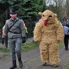 Barwny korowód na mięsopust: człowiek w stroju ze słomy i mężczyzna w kapeluszu idą obok siebie.