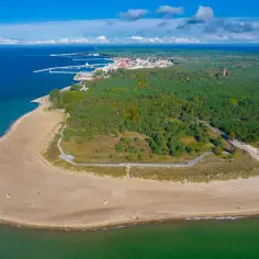 Malowniczy półwysep z piaszczystą plażą, lasem sosnowym i miasteczkiem portowym w oddali.