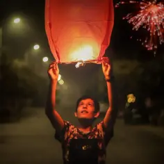 Chłopiec wypuszcza lampion życzeń w noc sylwestrową, podczas gdy fajerwerki rozświetlają niebo. Nowy rok w pełni!