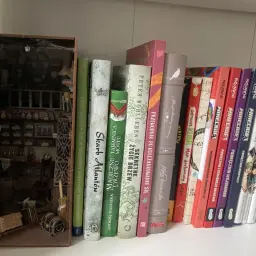 Miniaturowy book nook z detalami, jak z alchemicznej pracowni, obok kolorowych książek.